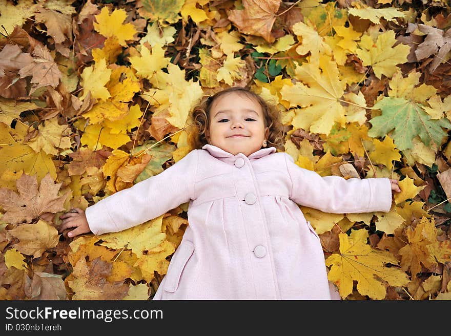 Little girl laying down on the leaves in the park in autumn. Little girl laying down on the leaves in the park in autumn