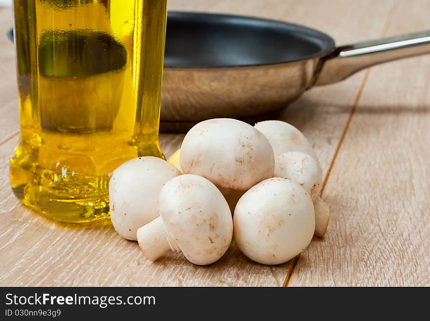 Button mushrooms, olive oil and frying pan on a wooden table. Button mushrooms, olive oil and frying pan on a wooden table