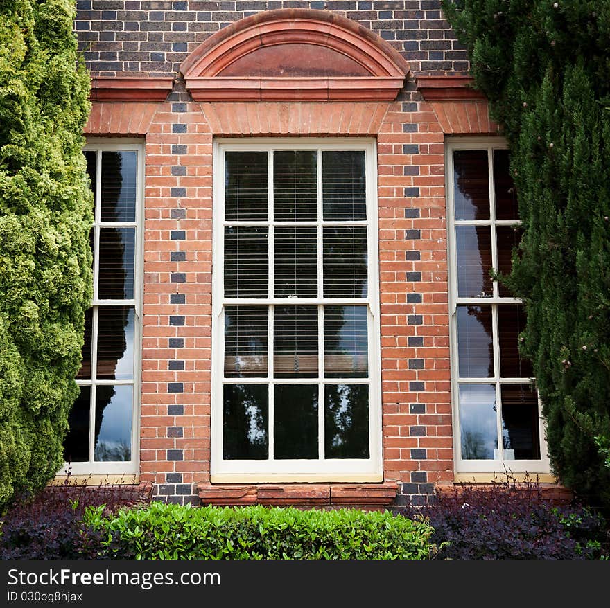 Windows in brick building framed by garden and fir trees. Windows in brick building framed by garden and fir trees.