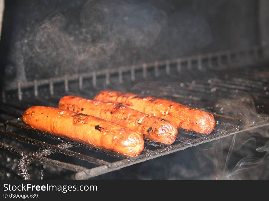 Hotdogs cooking on the grill in the summer time. Hotdogs cooking on the grill in the summer time.