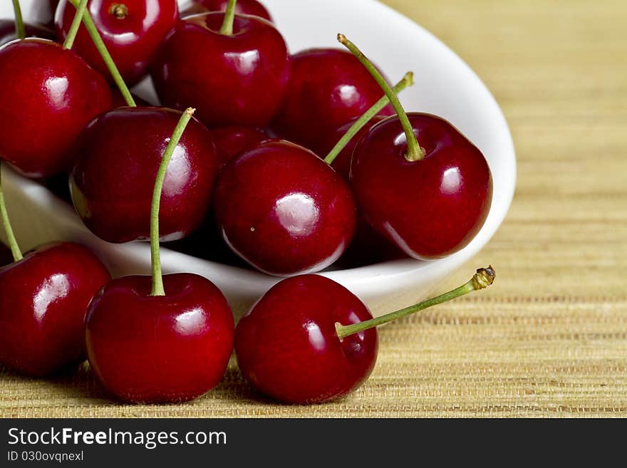 Red cherries in white spoon on yellow background