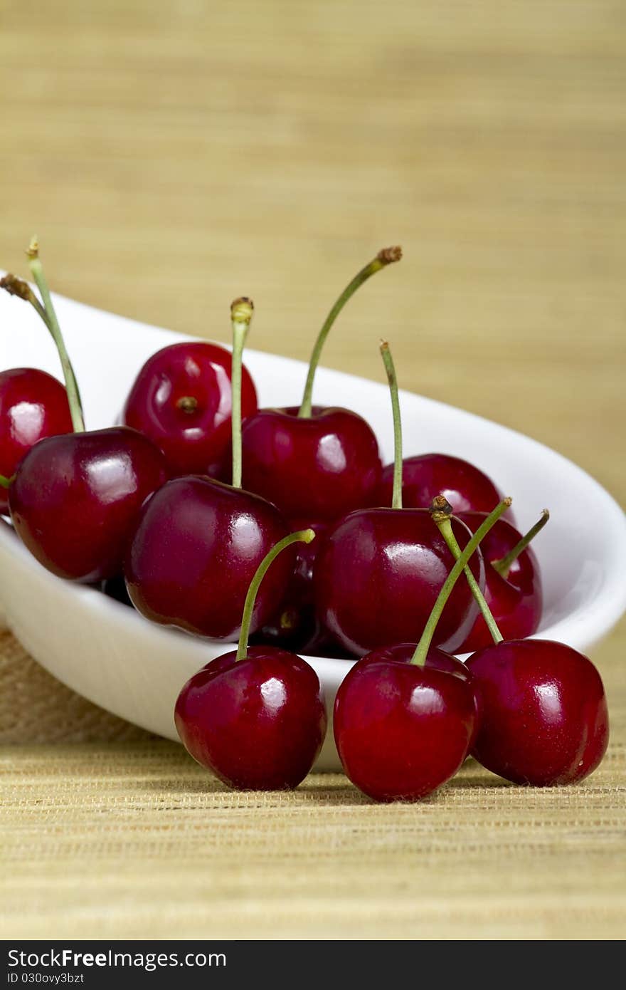 Fresh cherries in a white spoon on yellow background. Fresh cherries in a white spoon on yellow background