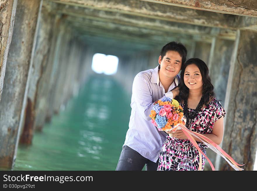 Couple standing outdoors smiling under pier on the beach. Couple standing outdoors smiling under pier on the beach