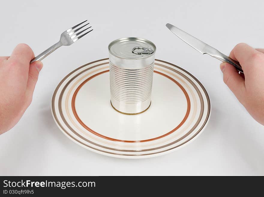 Man trying to eat the contain of the can with fork and knife. Man trying to eat the contain of the can with fork and knife.