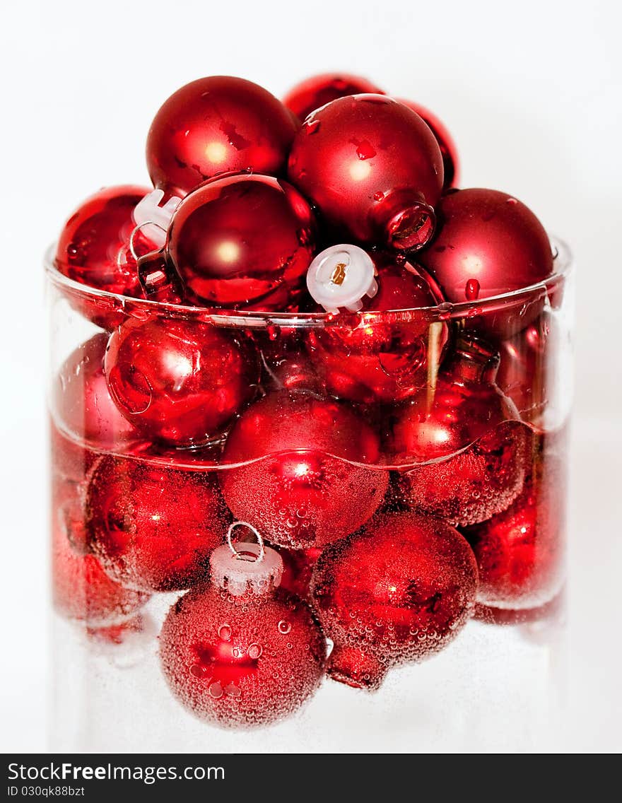 Clear glass cylinder holding a mound of red ball ornaments floating in water and covered with bubbles. Clear glass cylinder holding a mound of red ball ornaments floating in water and covered with bubbles