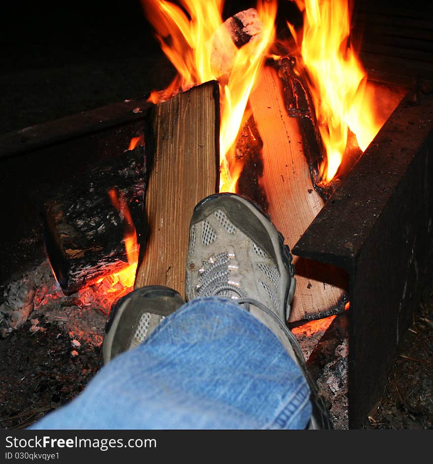 Legs and feet in hiking boots resting in front of a camp fire at night. Legs and feet in hiking boots resting in front of a camp fire at night