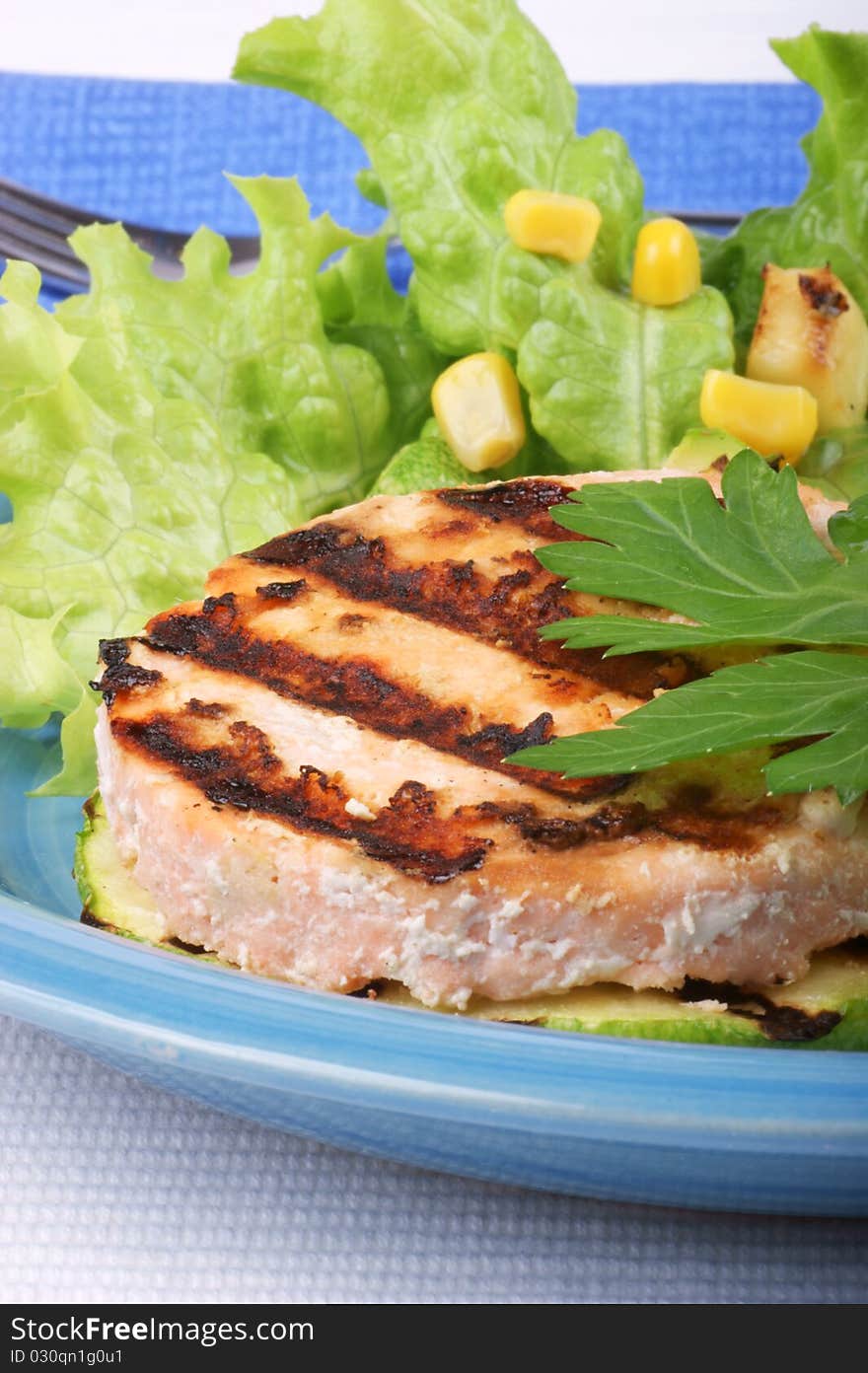 Grilled salmon and zucchini with salad and corn over a light blue plate. Studio shot. Shallow DOF. Grilled salmon and zucchini with salad and corn over a light blue plate. Studio shot. Shallow DOF