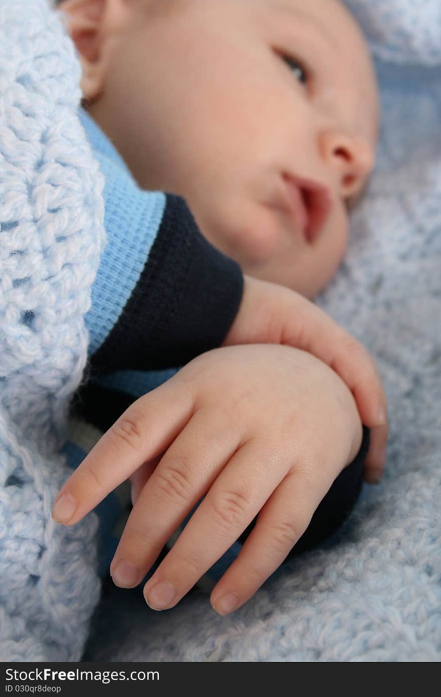 Two month old baby boy wrapped in a blanket. Focus on hand