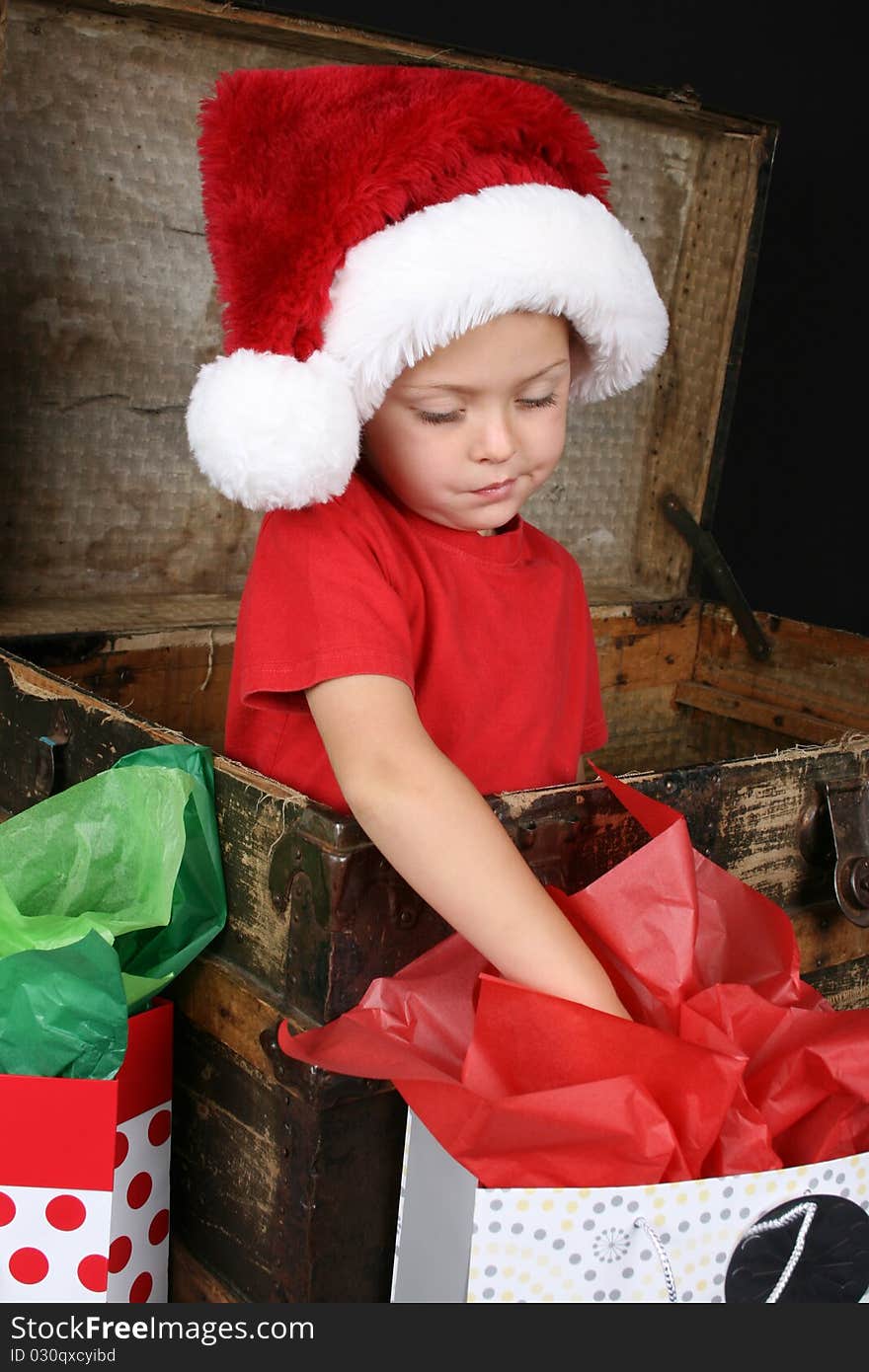 Little boy wearing a christmas hat looking inside the giftbag. Little boy wearing a christmas hat looking inside the giftbag