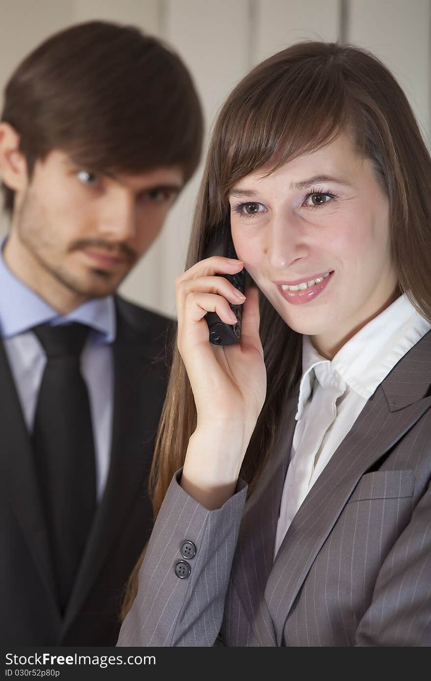 Businesswoman on phone in foreground - businessman to be ruled by jealousy. Focus on woman. Businesswoman on phone in foreground - businessman to be ruled by jealousy. Focus on woman