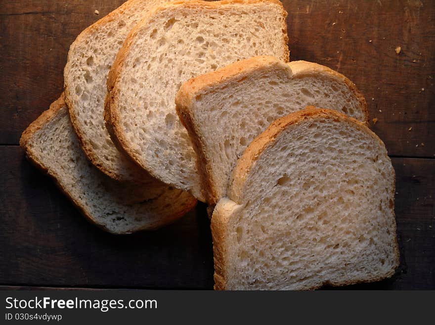 Few pieces of sliced white bread lying on dark wooden background. Few pieces of sliced white bread lying on dark wooden background