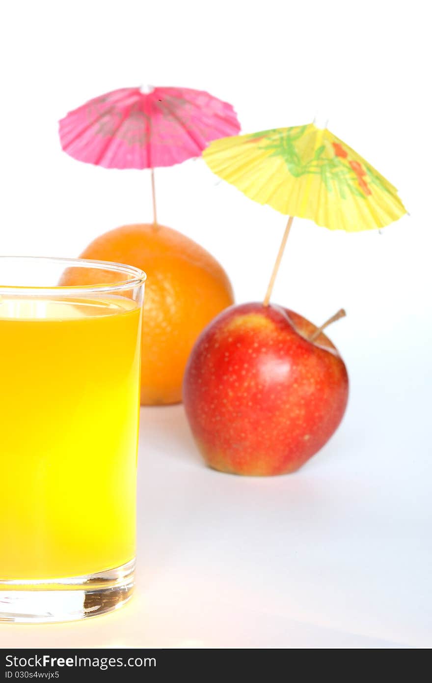 Orange and apple with small paper sunshades near glass of fruit juice on white background