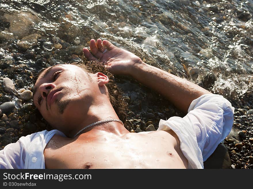 Young man lies on seacoast at water