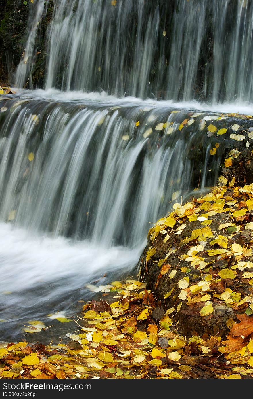 Waterfalls, a cascade of water flow, the stones are covered with fallen yellow leaves, autumn. Waterfalls, a cascade of water flow, the stones are covered with fallen yellow leaves, autumn