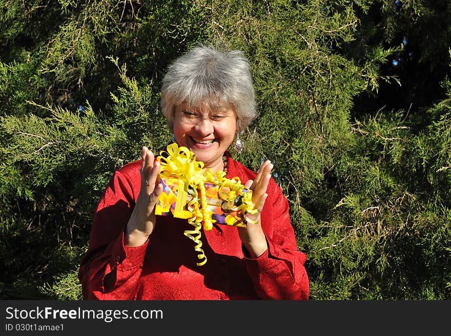 A happy, middle-aged woman holding a gift with both hands, against the backdrop of trees