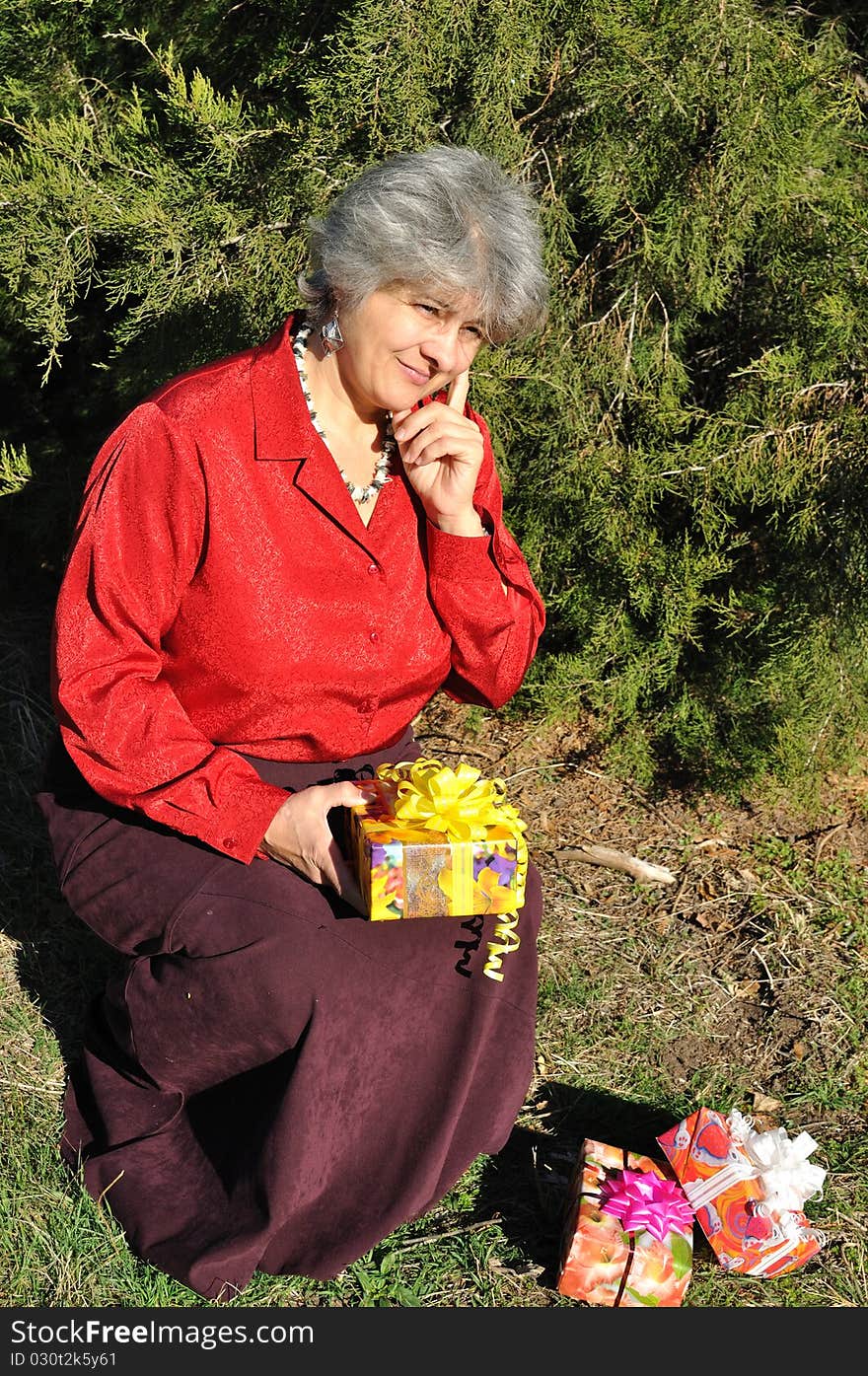 Puzzled, the old woman holds a lot of gifts, amid trees