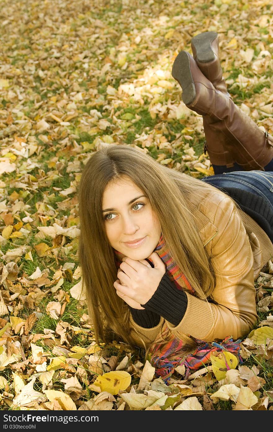 Portrait of a beautiful young woman, lying in a pile of leaves, smiling, looking up. Portrait of a beautiful young woman, lying in a pile of leaves, smiling, looking up