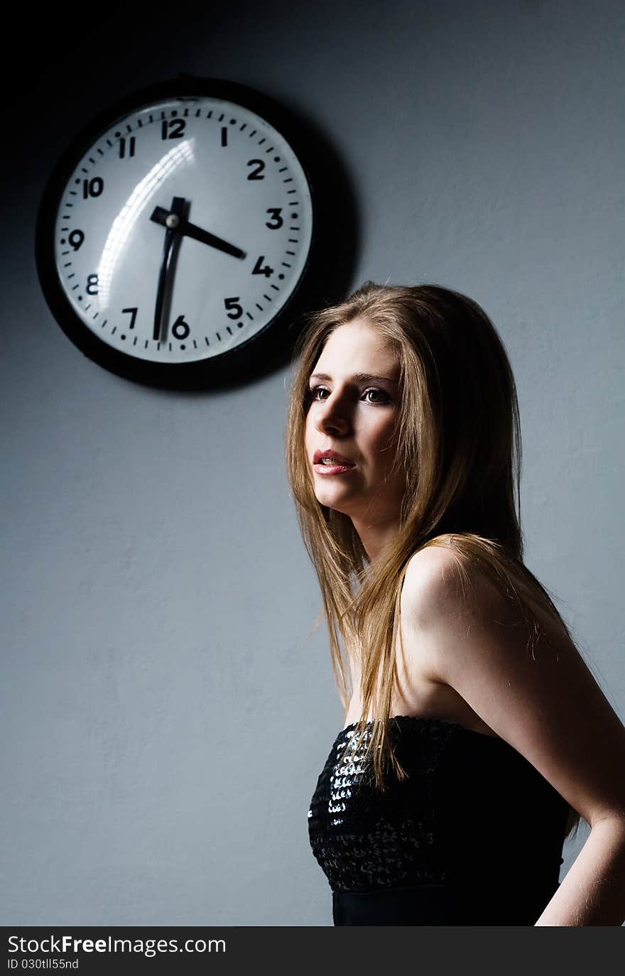 Attractive young woman and clock on gray background