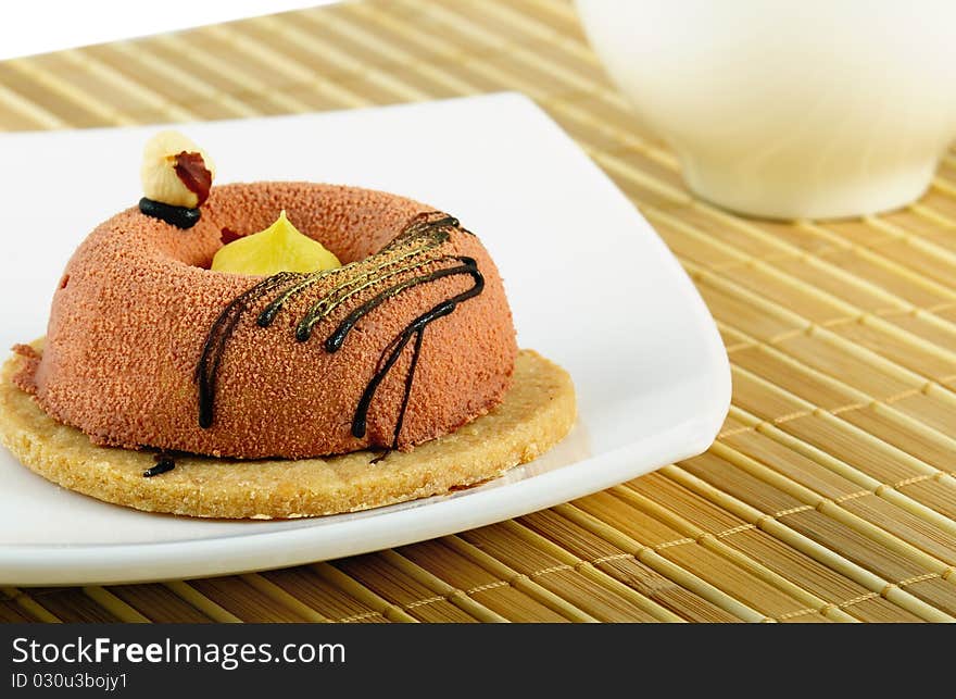 The cake lays on a white plate. On a background the white cup is located. Closeup. The cake lays on a white plate. On a background the white cup is located. Closeup