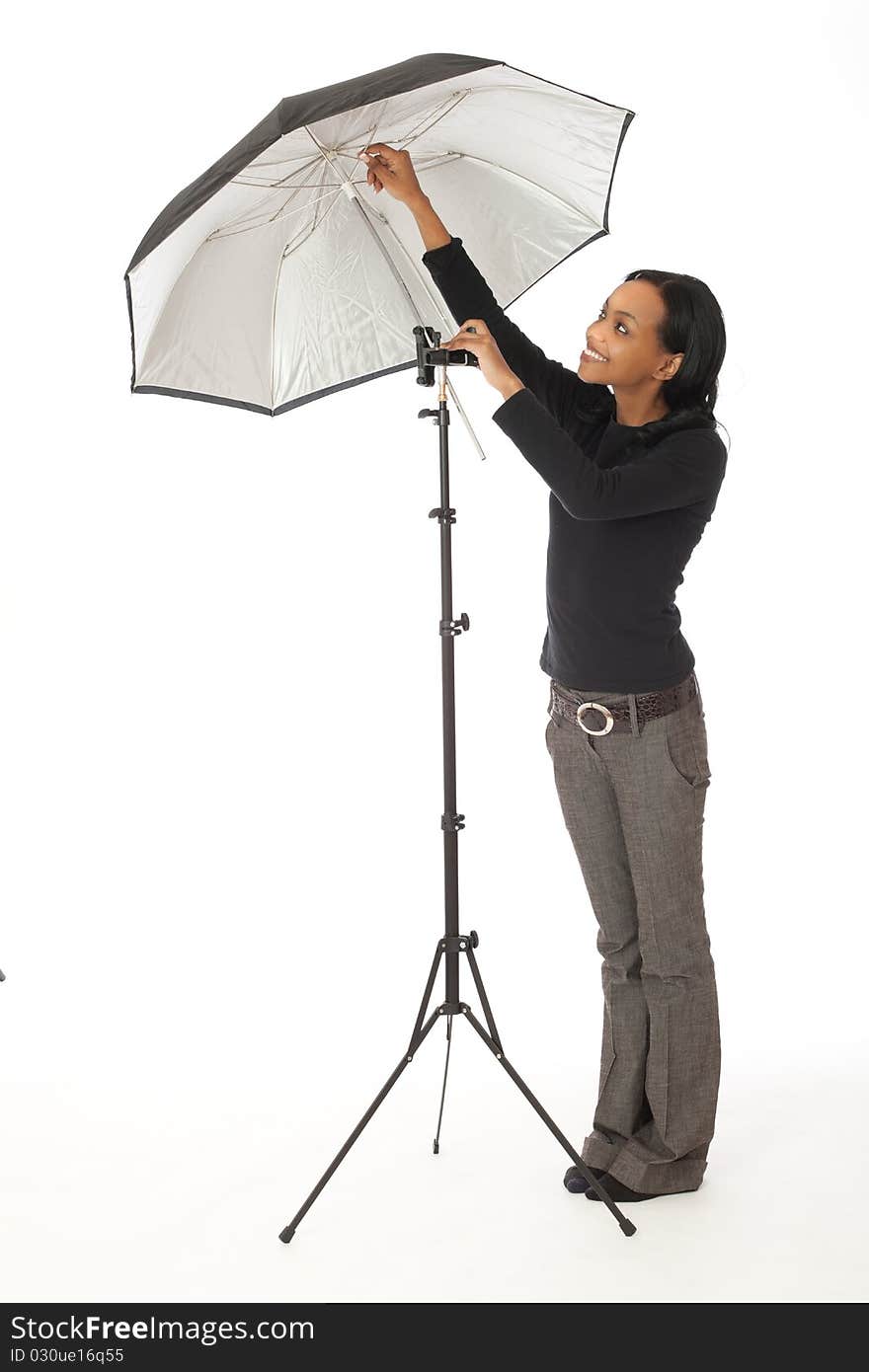 Pretty female photographic assistant adjusting photographic umbrella in studio