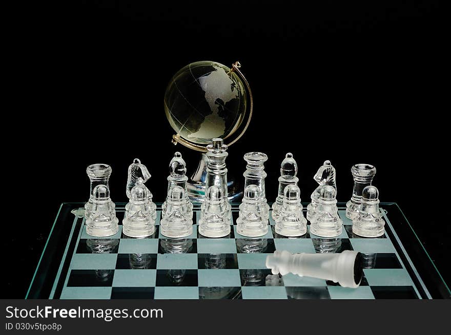 Crystal chess pieces with a globe in the background ana fallen king. Crystal chess pieces with a globe in the background ana fallen king.