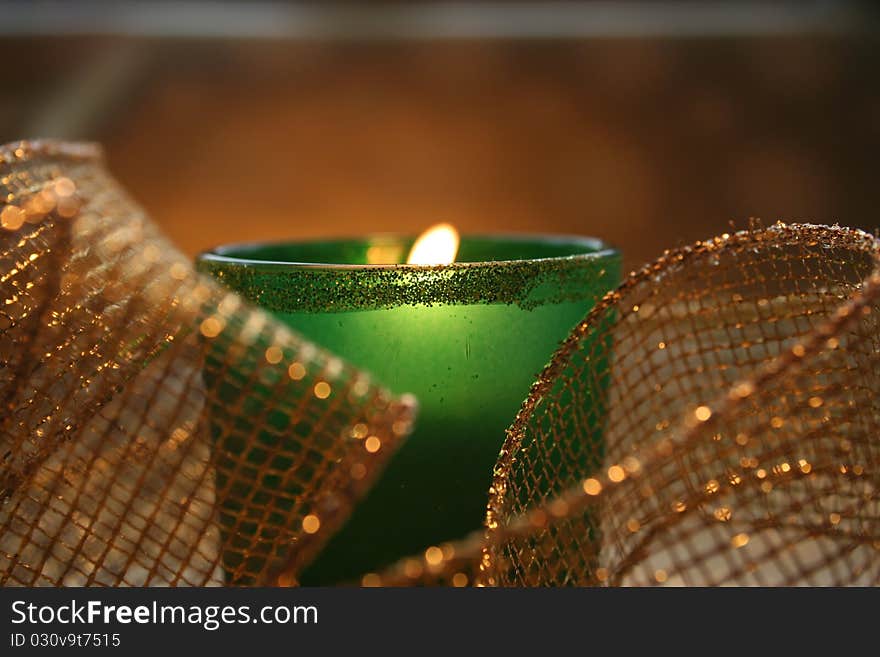 Closeup of a candle burning in a green glass votive holder surrounded by gold mesh ribbon. Closeup of a candle burning in a green glass votive holder surrounded by gold mesh ribbon.