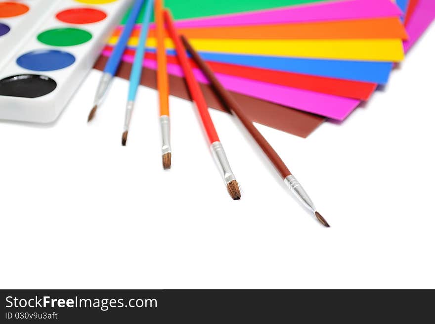 Brushes, paints and a color paper for creativity over white