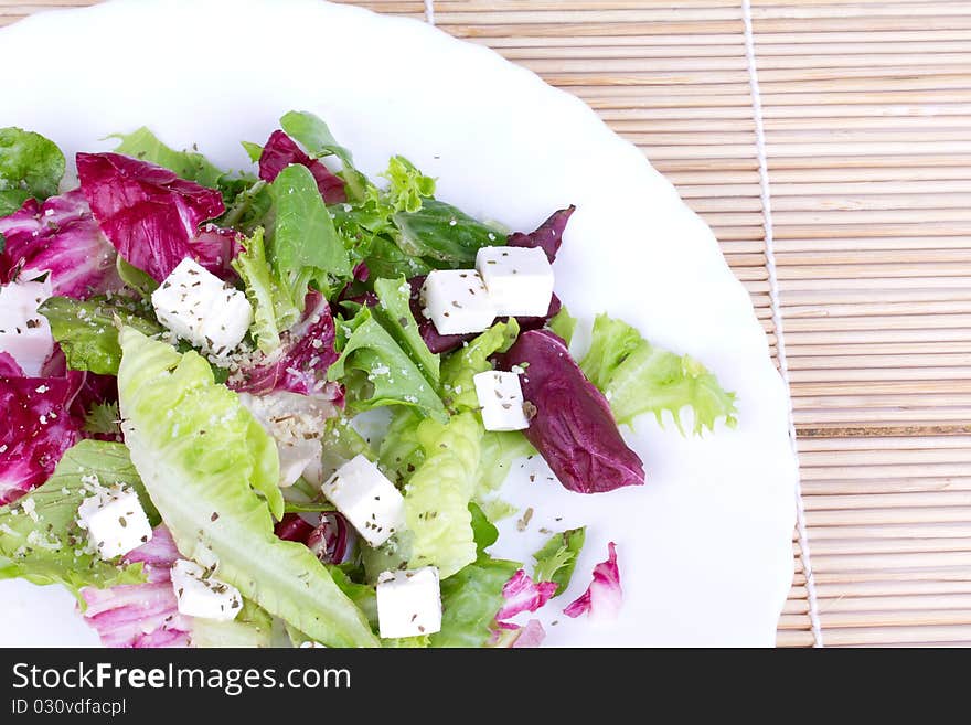 Salad with leafs and sheep cheese on plate,closed-up on wooden mat