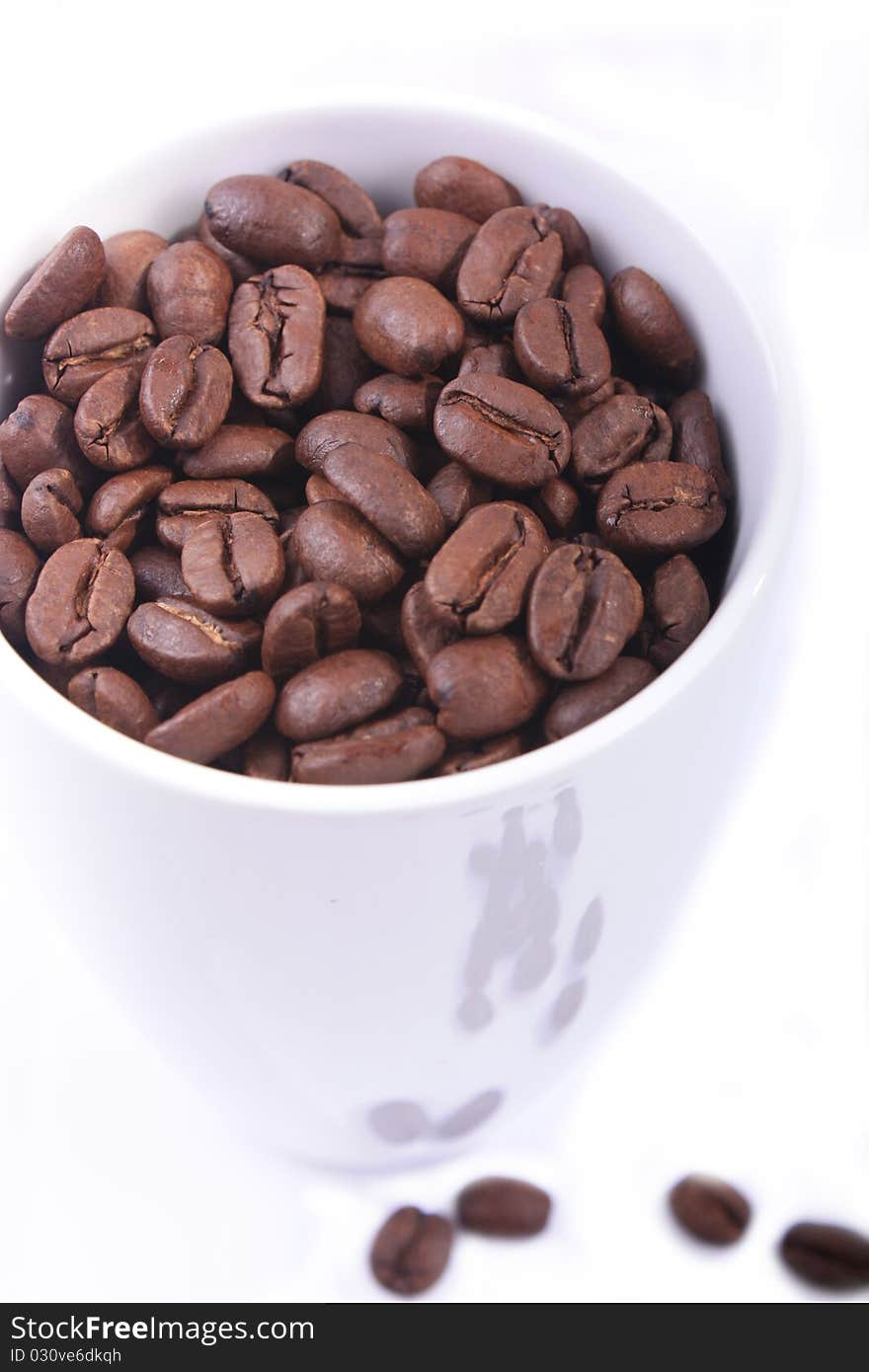 Coffee beans side a coffee cup,with that have spilt over on a white background. Coffee beans side a coffee cup,with that have spilt over on a white background