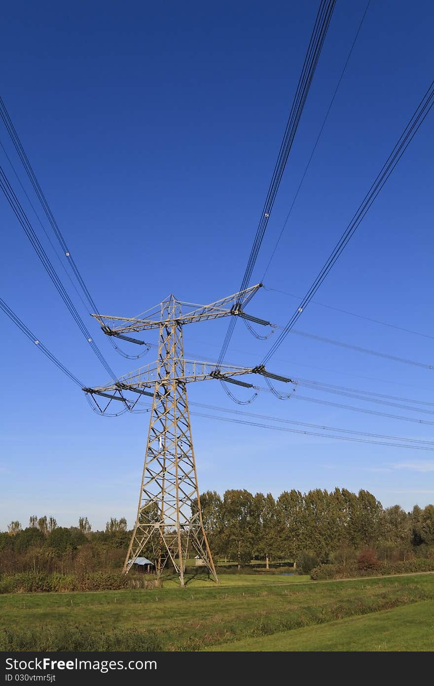 Electricity pylon in perspective against a deep blue sky standing in a green field. Electricity pylon in perspective against a deep blue sky standing in a green field