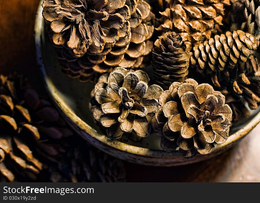 A pottery bowl filled with pine cones and sitting on a wooden table indoors. A pottery bowl filled with pine cones and sitting on a wooden table indoors.