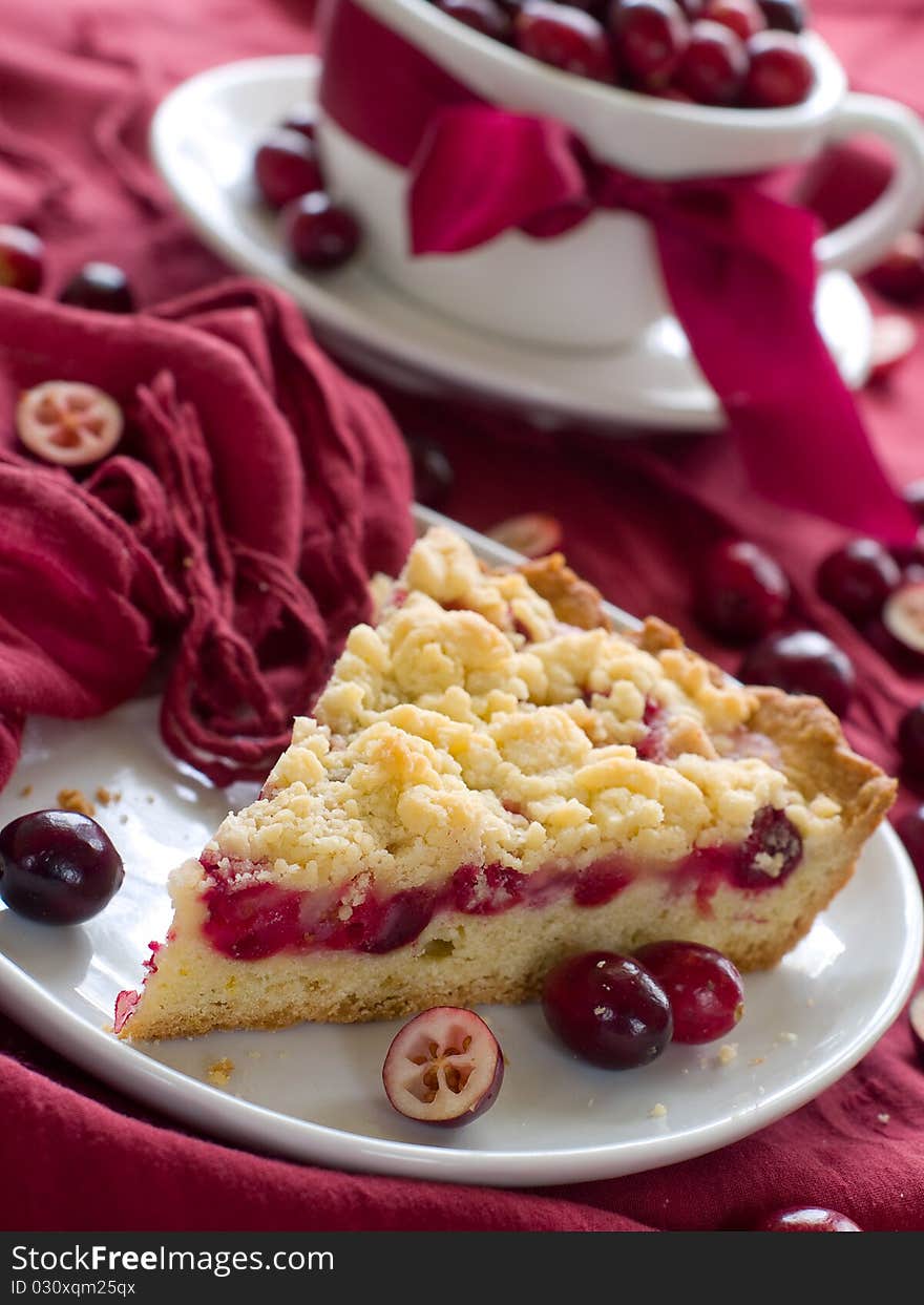 Piece of cranberry cake with cup of cranberry on background