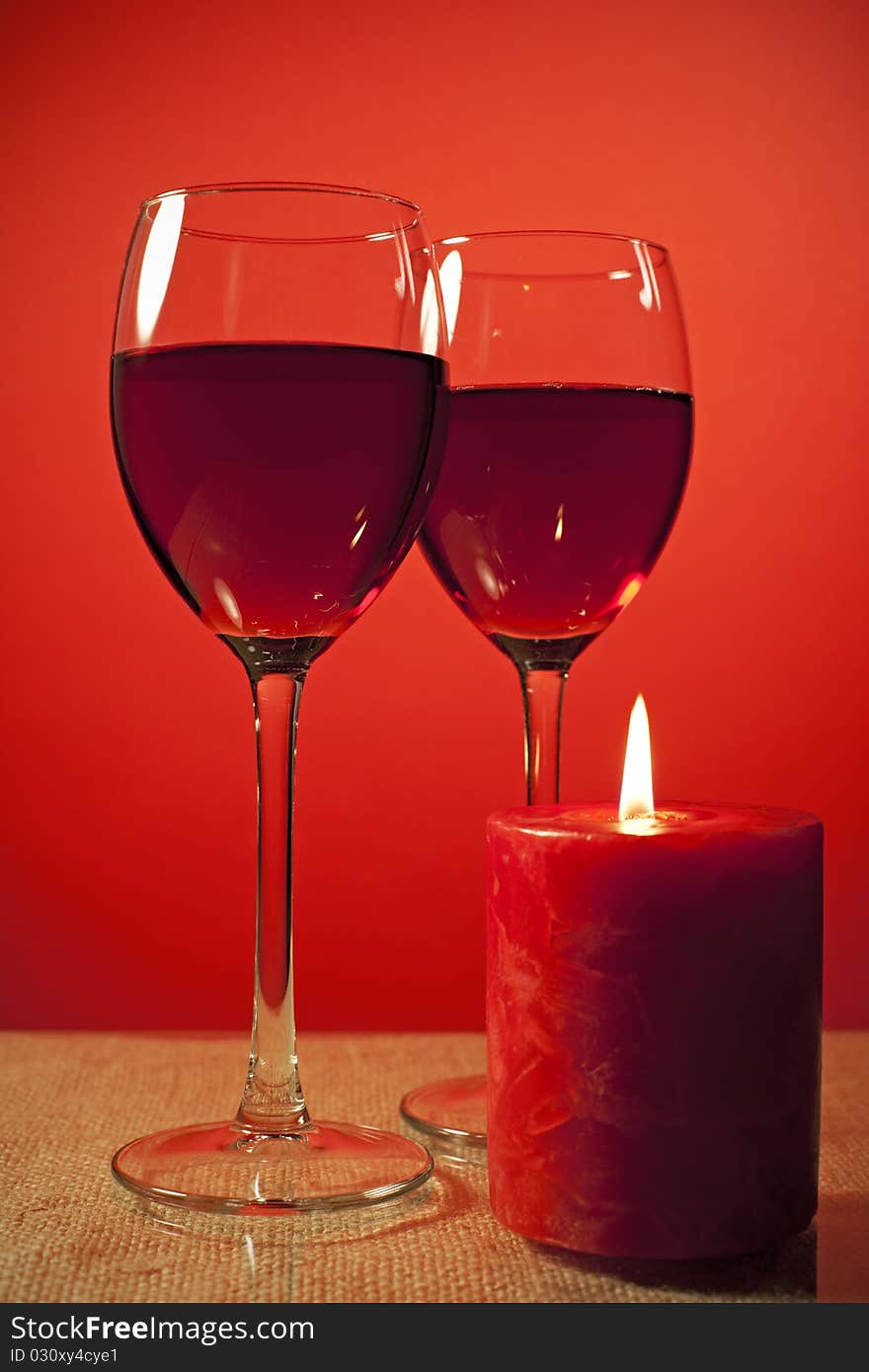 Two Glass of wine and a candle over red background