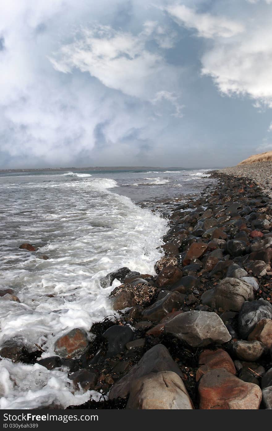 A pebbled beach on a bright day with calm sea waves splashing against the pebbles as a background. A pebbled beach on a bright day with calm sea waves splashing against the pebbles as a background