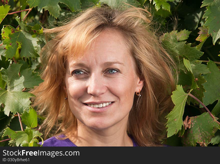 Blue-eyed woman in a blue shirt on the background of vine leaves. tousled blond hair.