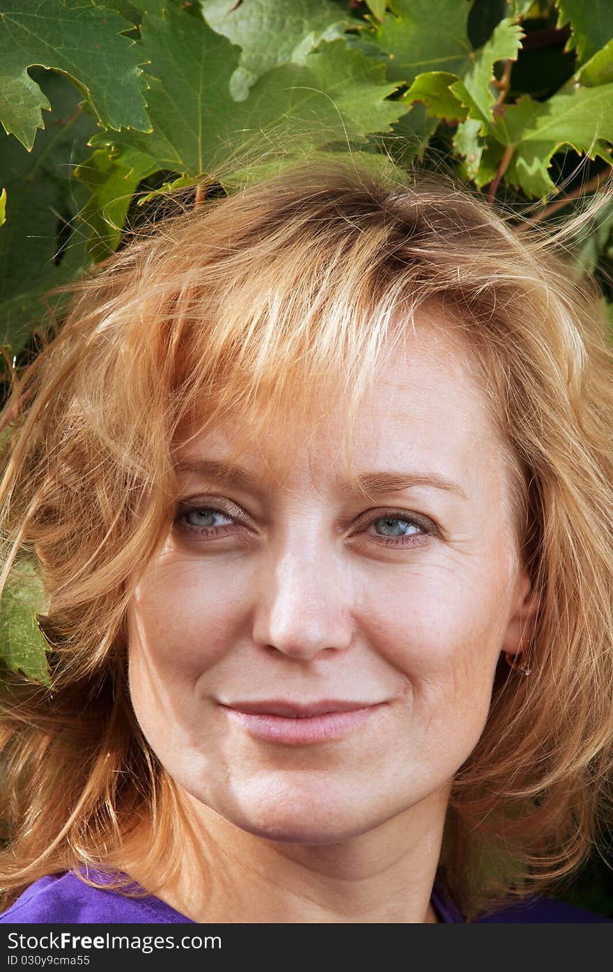 Blue-eyed woman in a blue shirt on the background of vine leaves. tousled blond hair.