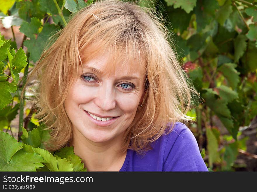 Blue-eyed woman in a blue shirt on the background of vine leaves. tousled blond hair.