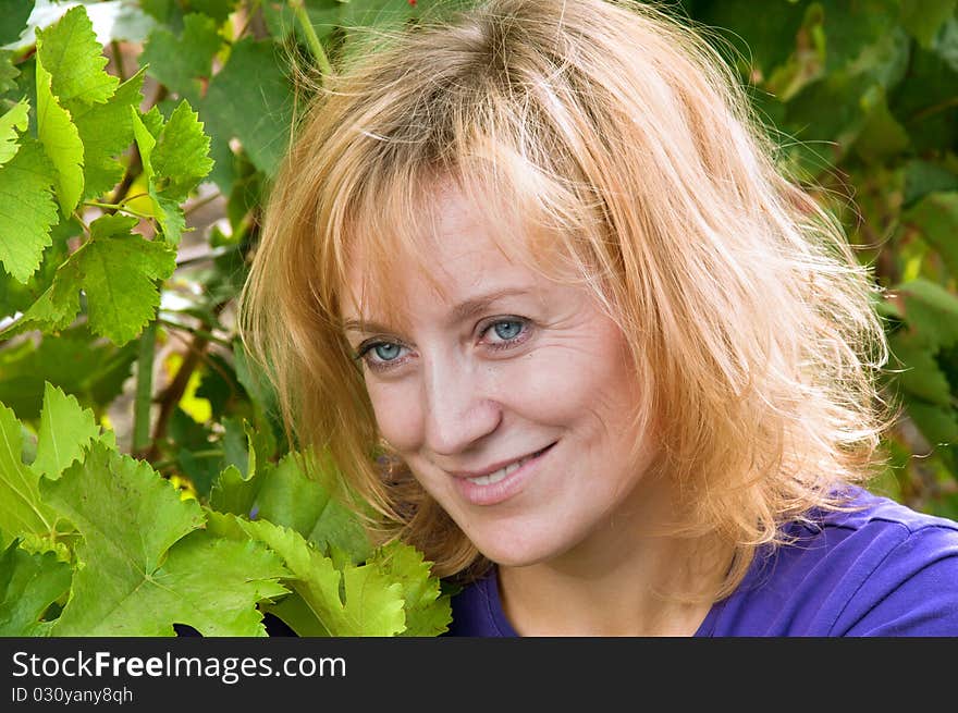 Blue-eyed woman in a blue shirt on the background of vine leaves. tousled blond hair.