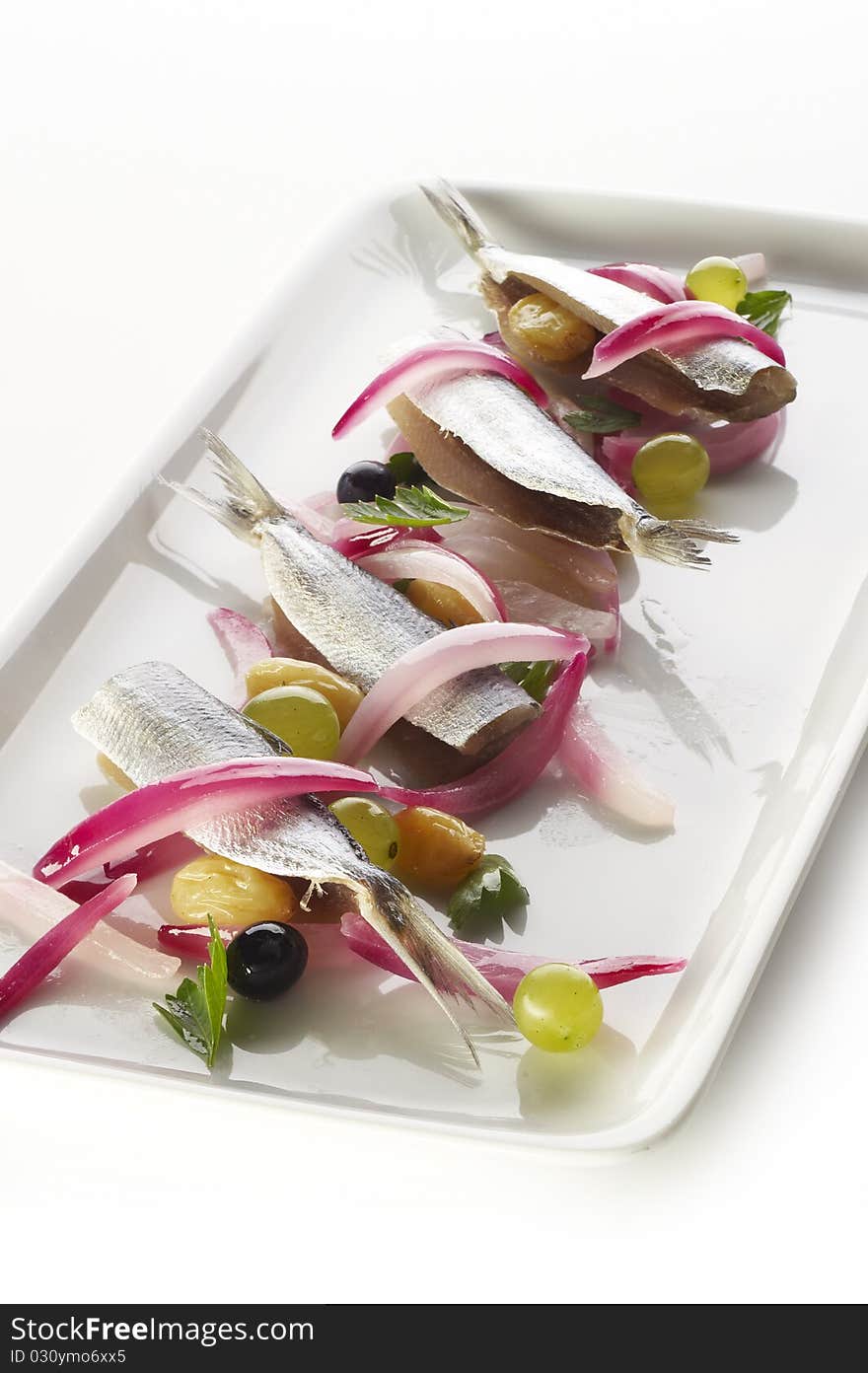 Sardines with grapes and red onion on white plate