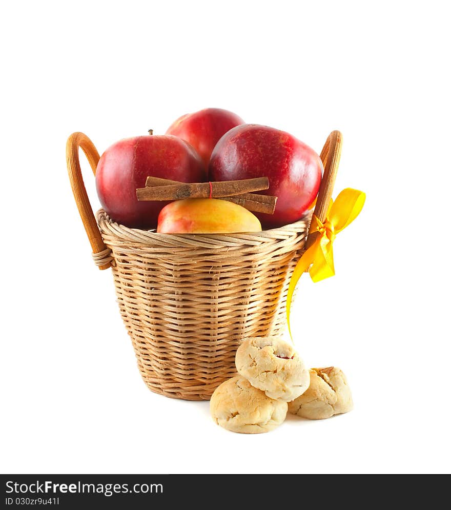 Red apples in a basket with cookies and cinnamon. Isolated on white background