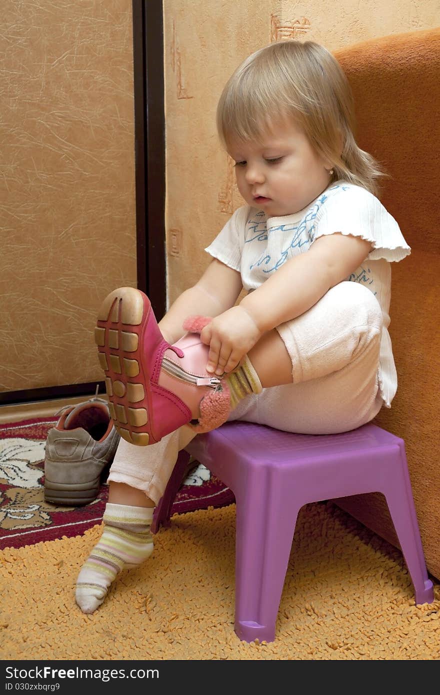 The small child sits near a door and puts shoes on. The small child sits near a door and puts shoes on