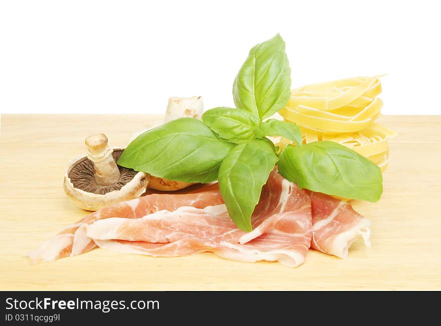 Fresh basil herb leaves,mushrooms, parma ham and tagliatelle on a wooden board. Fresh basil herb leaves,mushrooms, parma ham and tagliatelle on a wooden board