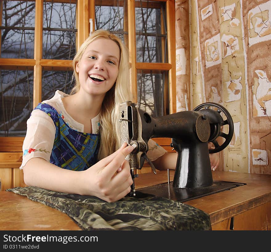 Young woman sitting at a sewing machine in the farmhouse. Young woman sitting at a sewing machine in the farmhouse.