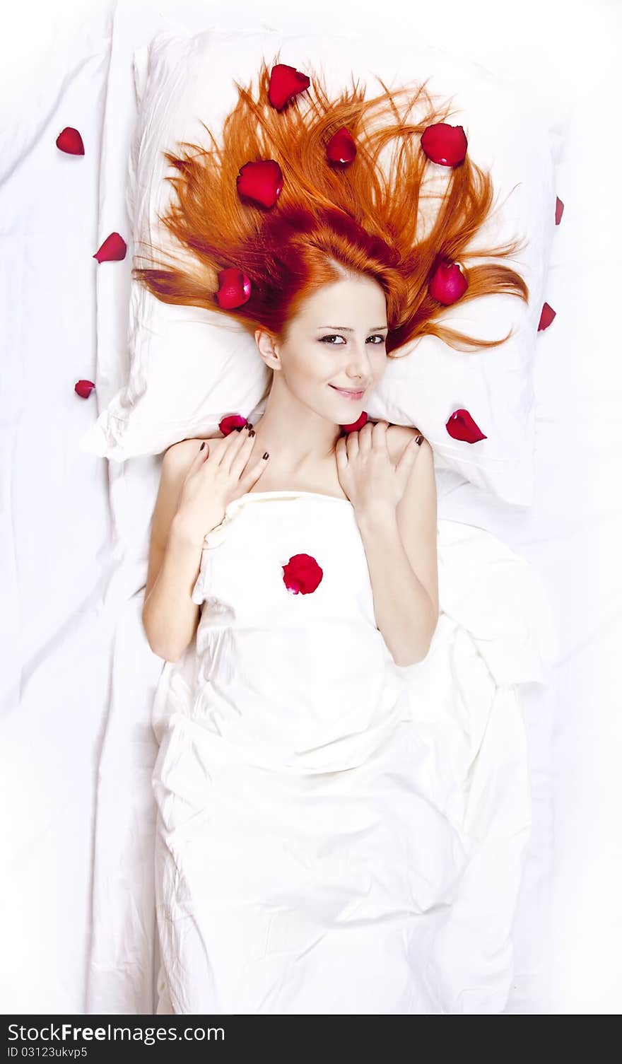 Beautiful red-haired girl in bed with rose petal. Studio shot.