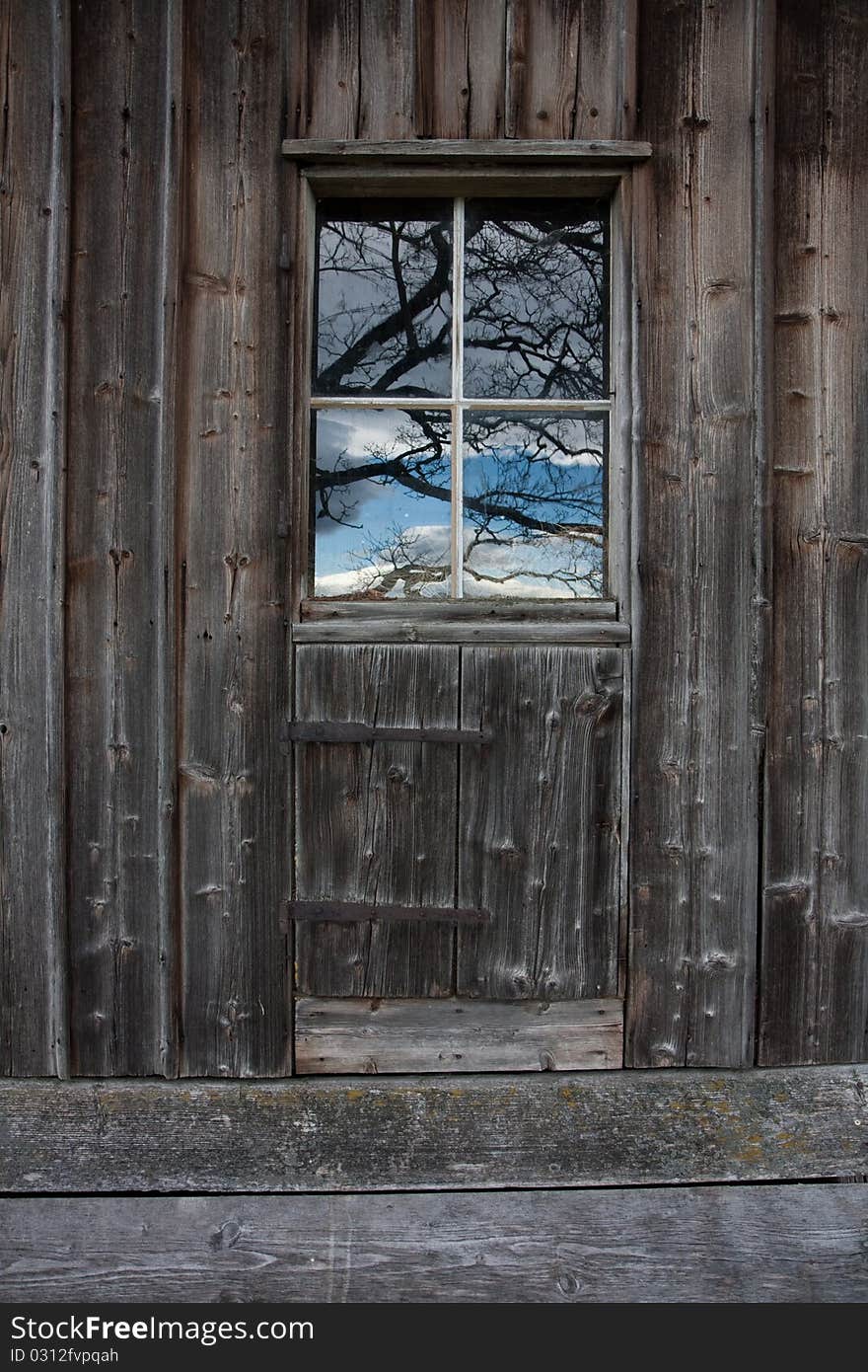 Old woodshed with reflection of sky and tree brunches in a window. Old woodshed with reflection of sky and tree brunches in a window