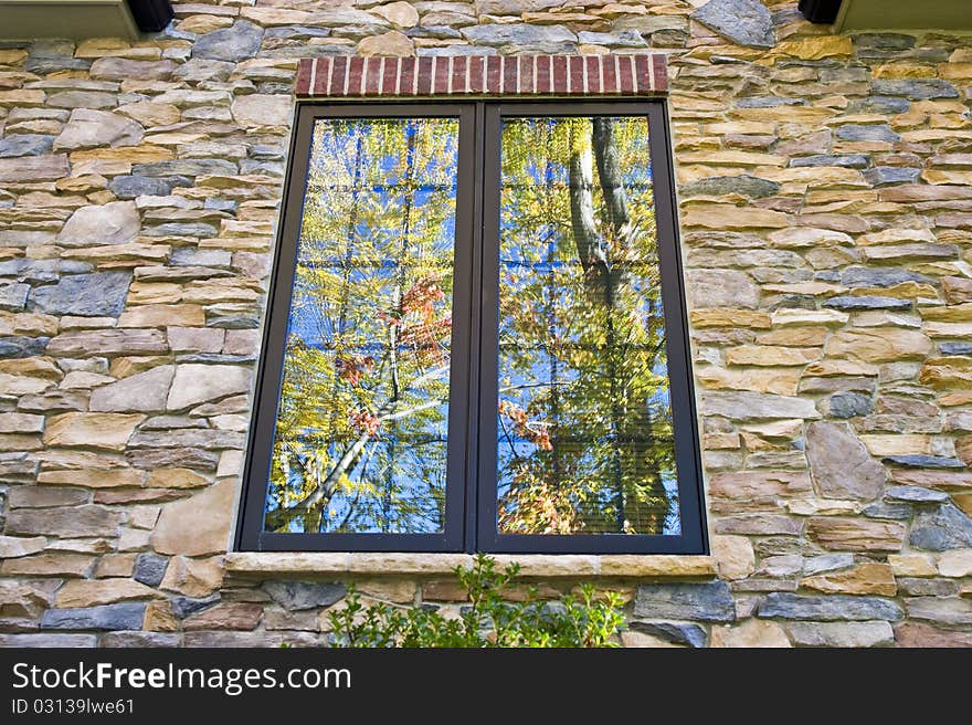 Trees with yellow, orange, and green leaves reflected in a window on a brick wall. Trees with yellow, orange, and green leaves reflected in a window on a brick wall