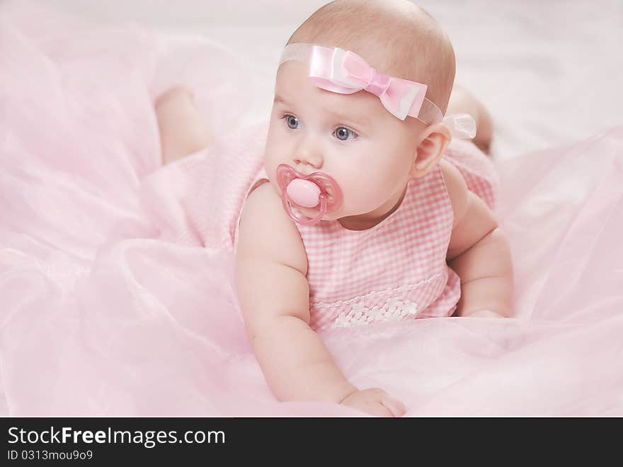 Portrait of a little baby on a soft blanket with a pacifier and pink bow