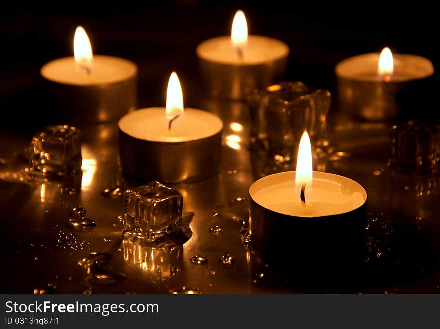 Five lighted candles with melting ice cubes and water drops