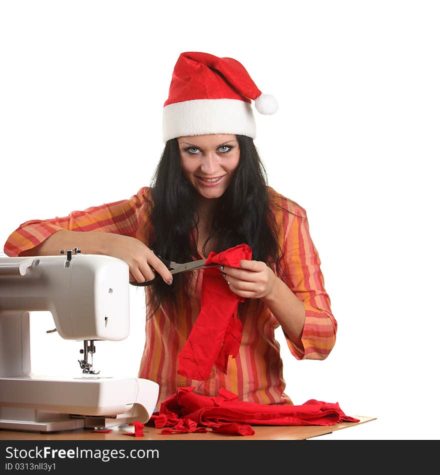 Beautiful woman seamstress in a Christmas hat cut red cloth by scissors. Beautiful woman seamstress in a Christmas hat cut red cloth by scissors