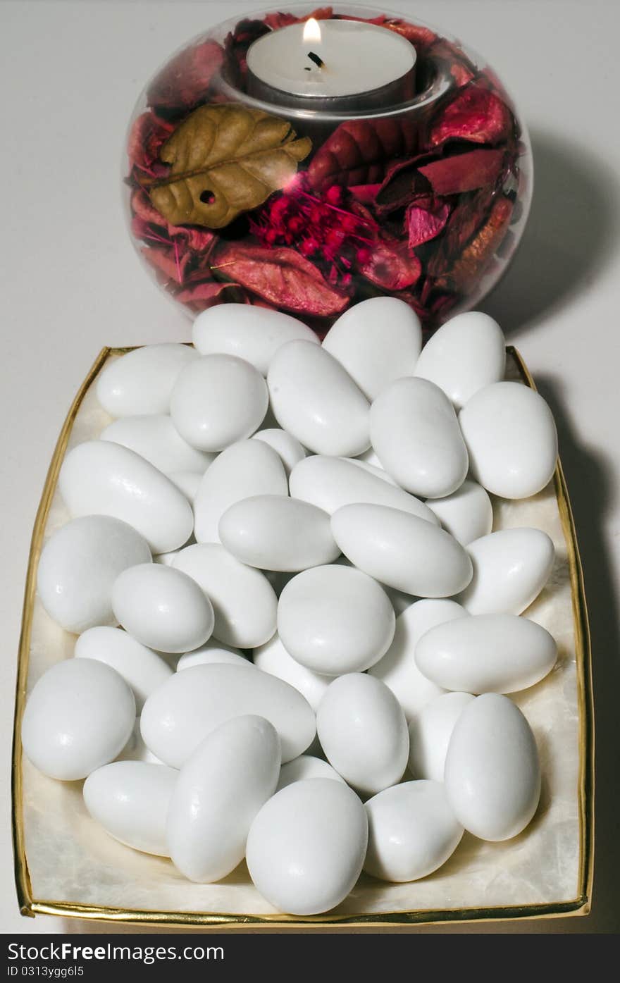 A plate filled with sugared almonds and a lighted wax candle. A plate filled with sugared almonds and a lighted wax candle